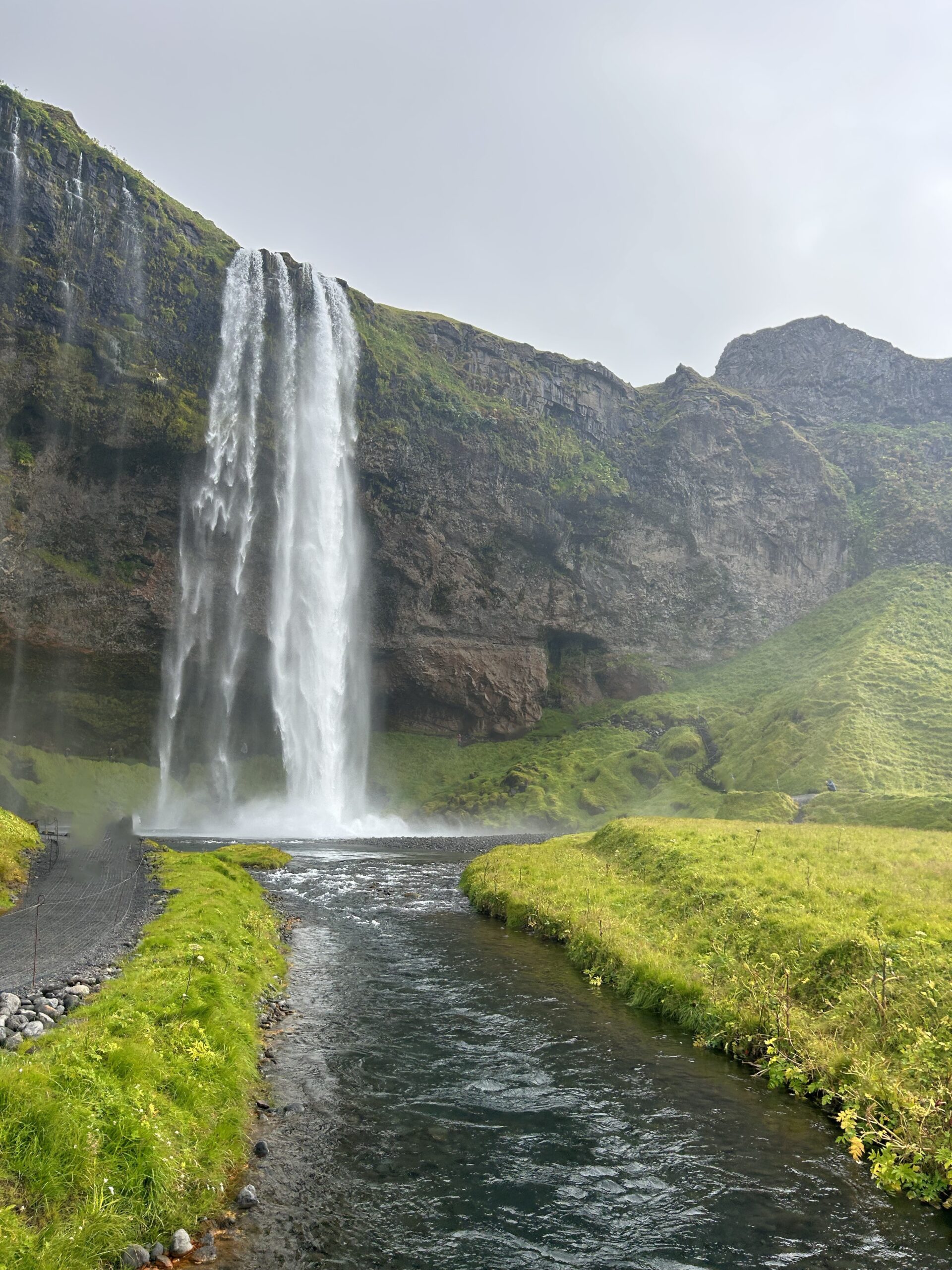 Seljalandsfoss waterfall cascades dramatically over rocky cliffs, creating a misty atmosphere on the surrounding black sand landscape.