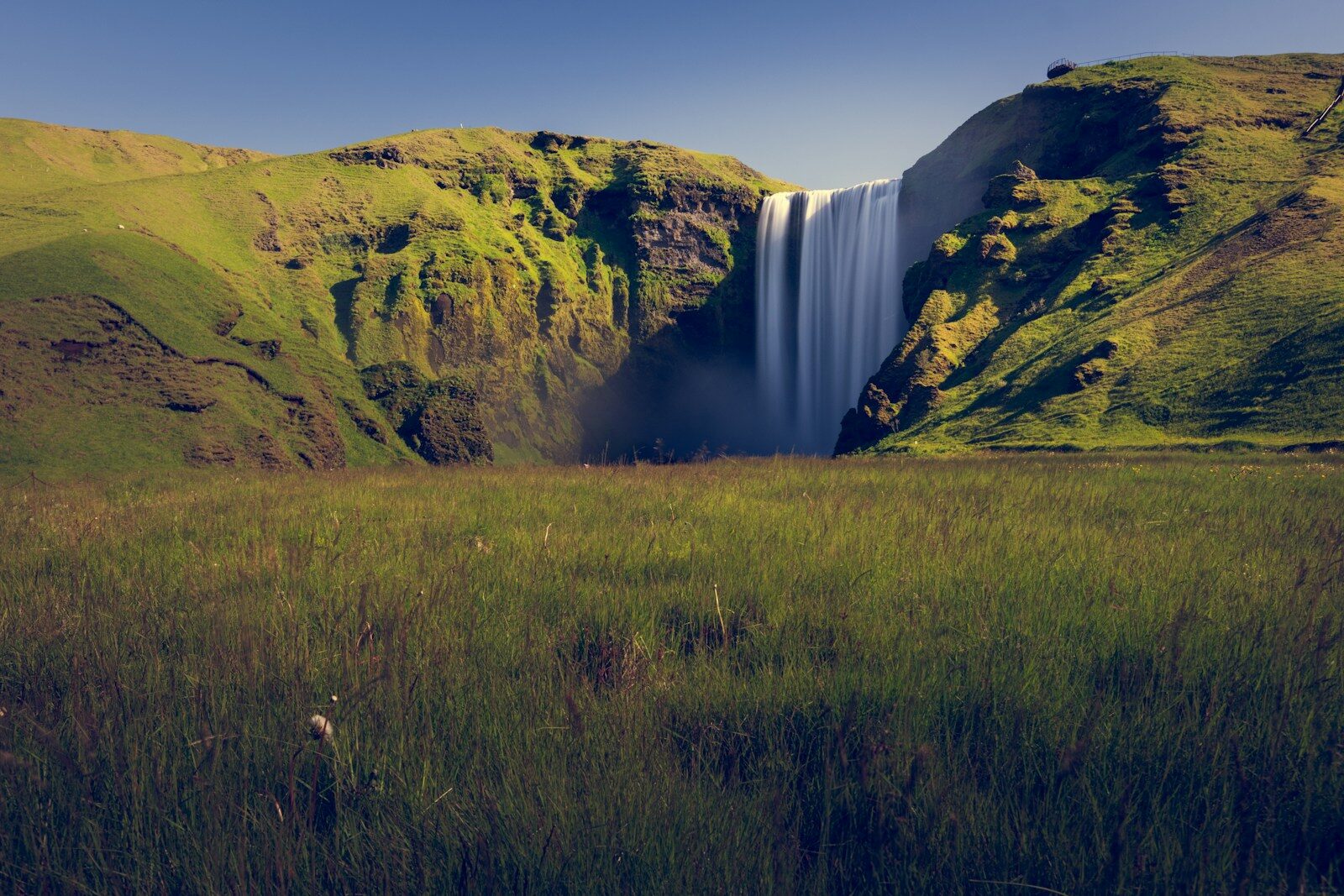 A majestic waterfall cascades down a green hill.